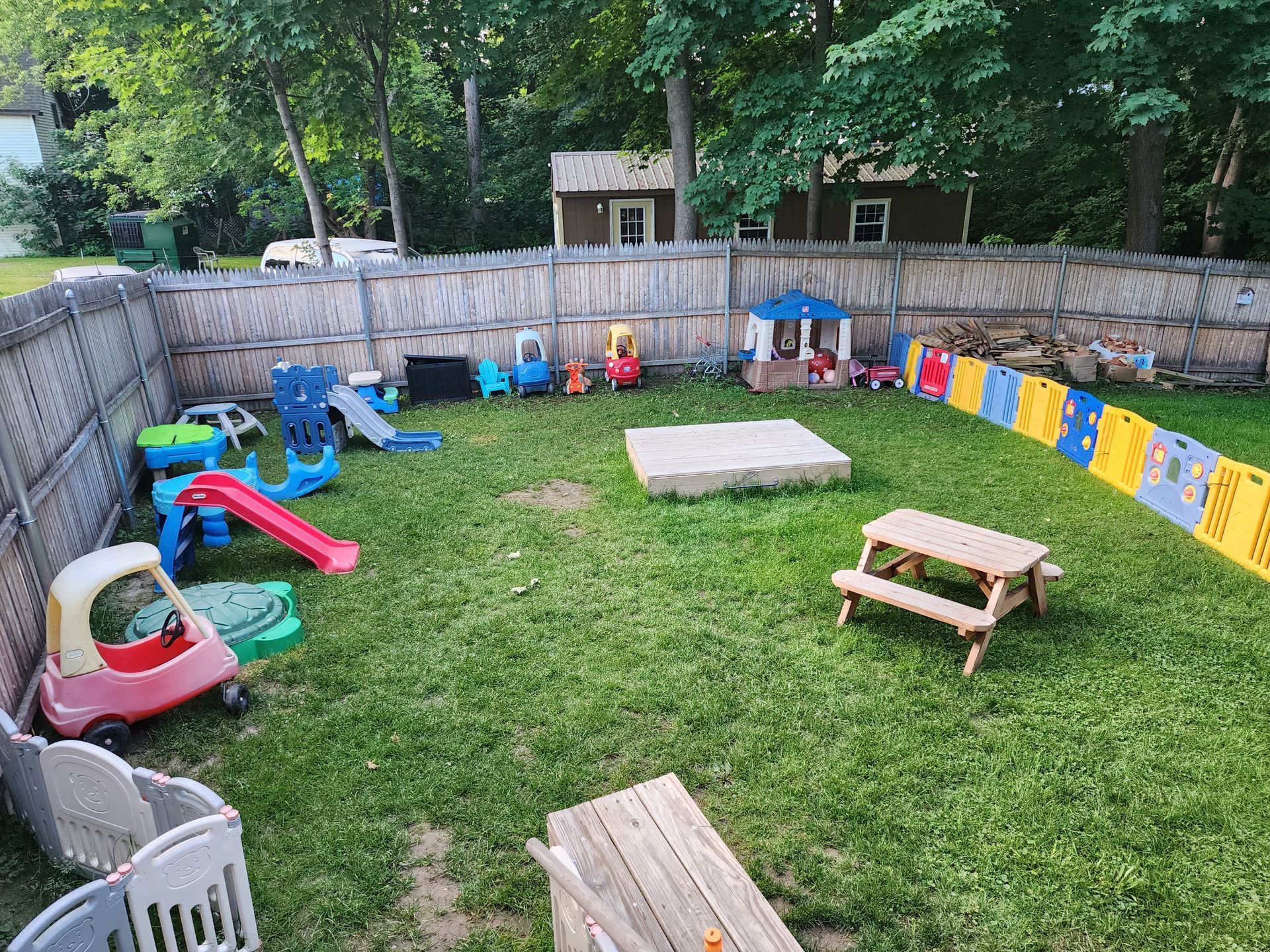 Children’s backyard playground with colorful play equipment, grass, and a small picnic table near a fenced yard
