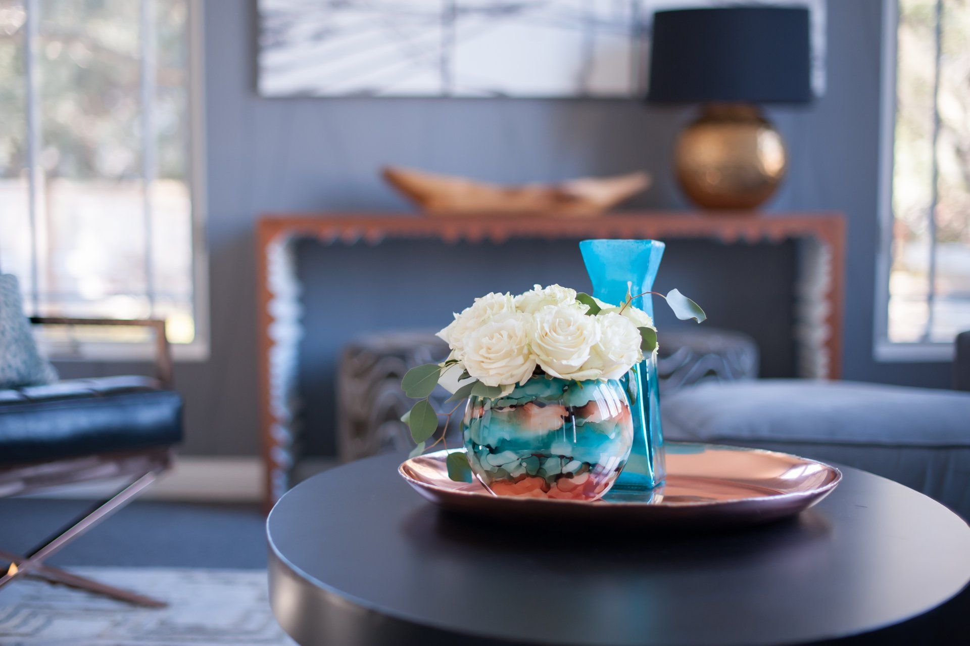 A vase of flowers is on a tray on a table in a living room.