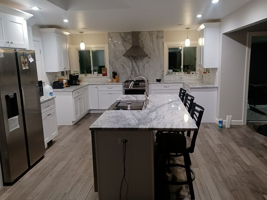 A kitchen with white cabinets , stainless steel appliances , marble counter tops and a large island.