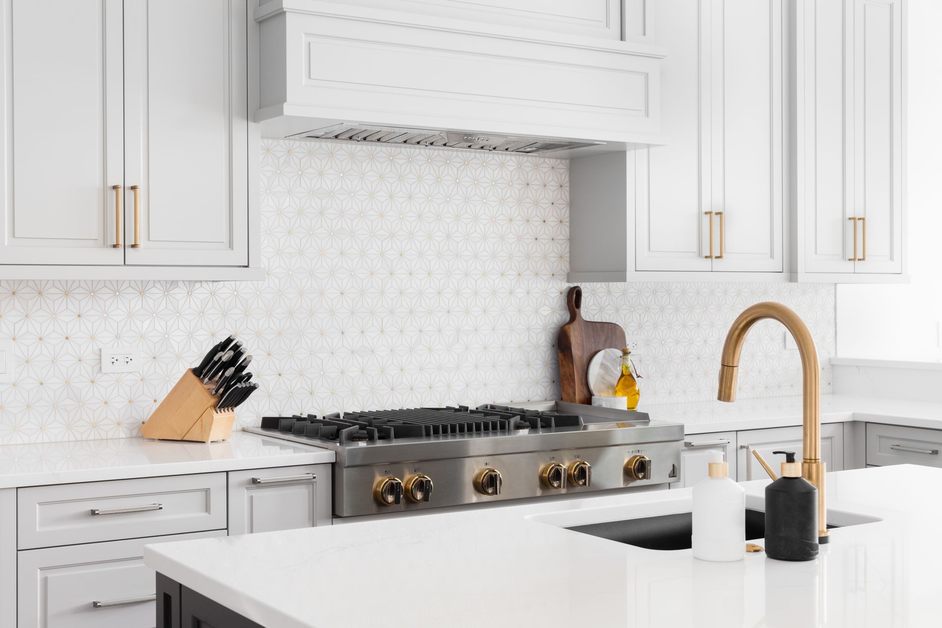 A kitchen with white cabinets , a stove , a sink , and a faucet.