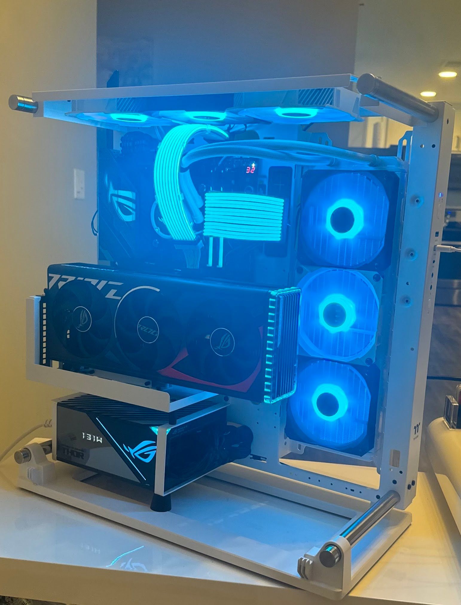 Open-frame gaming PC case with blue LED-lit fans and visible graphics card on a desk