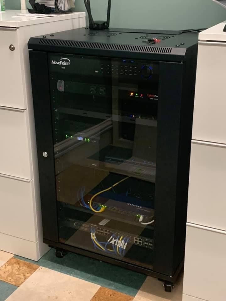 Black server rack cabinet with glass door in a utility room, showing network equipment inside.