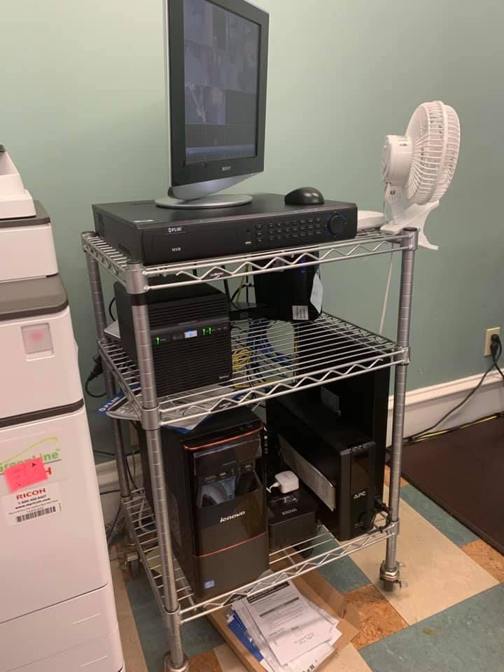 Computer workstation on a metal cart with monitor, keyboard, and fan in an office corner