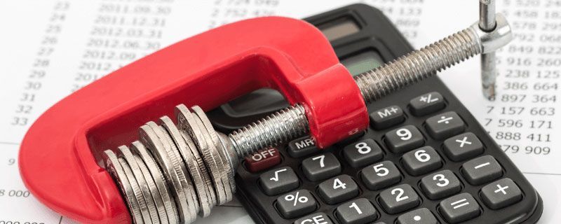 Red clamp squeezing coins and calculator on financial papers.