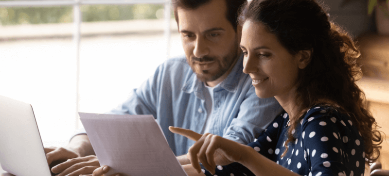 Man and woman review documents together. Woman points to a paper, both smiling.