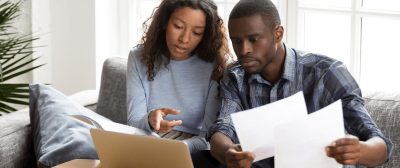 A couple looking at papers and a laptop while seated on a couch.