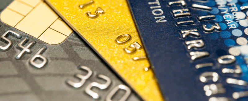 Close-up of three credit cards in gray, yellow, and blue. Numbers and chip are visible.