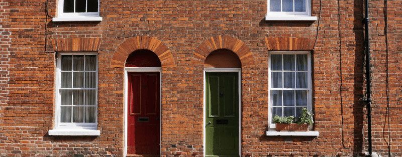 Two brick townhouses, with a red and green door, framed by arched brickwork, windows above.