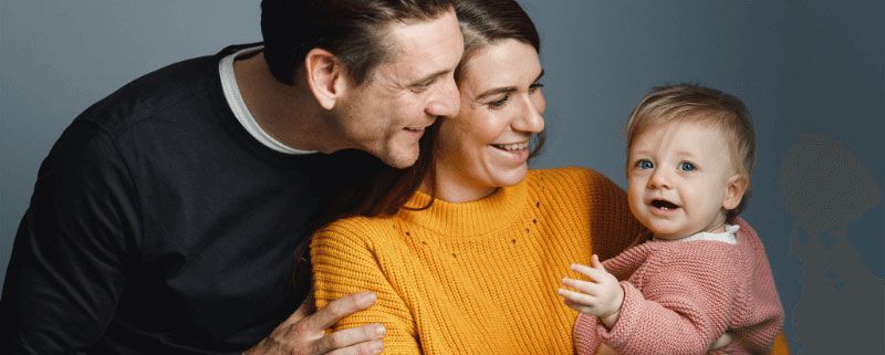 A family of three, with the parents holding a baby. The baby is crying.