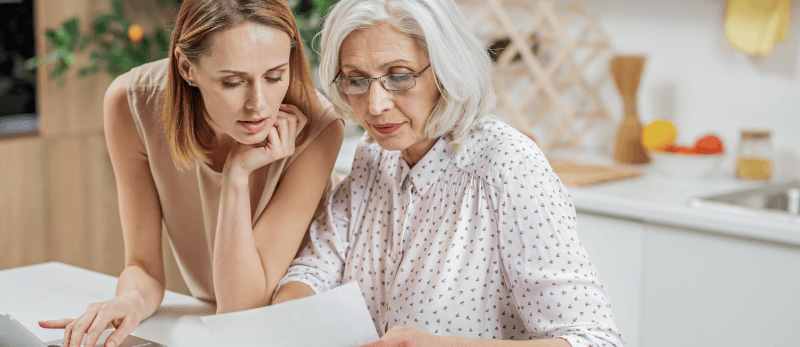 Woman and senior woman reviewing paperwork in kitchen.