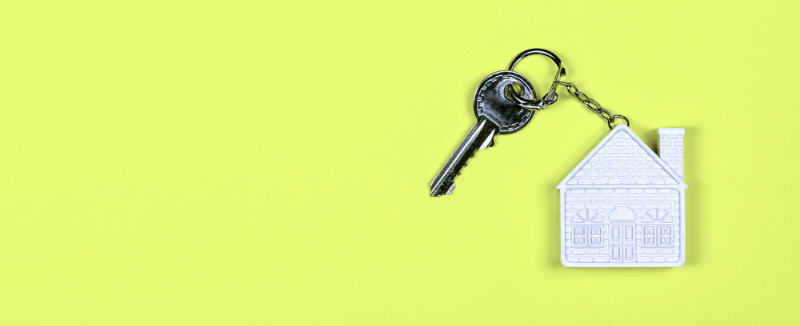 Key with a house-shaped keychain on a yellow background.