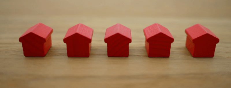 Five red wooden houses in a row on a wooden surface.