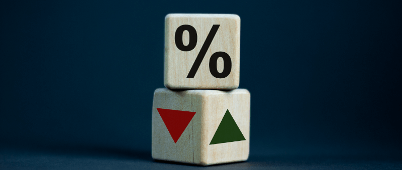 Two wooden blocks stacked; one with a percentage sign on top, the other with red down arrow and green up arrow.
