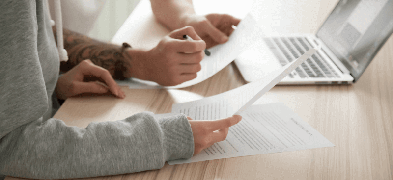 Two people reviewing documents together; laptop on a light wooden surface.