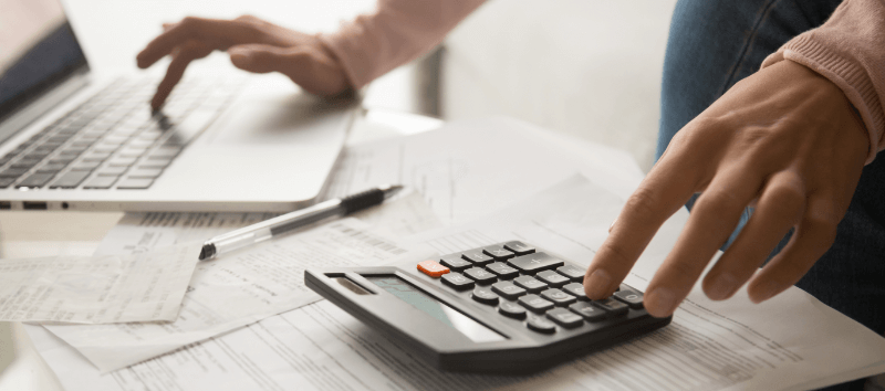 Person using a laptop and calculator, working on financial documents.