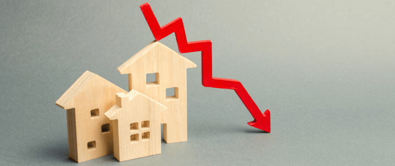 Wooden houses with a red downward arrow, symbolizing a housing market decline.