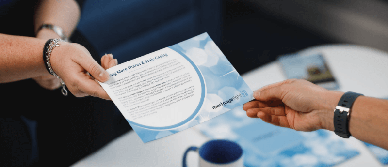 Person handing a brochure to another person. The brochure has a blue design and text.