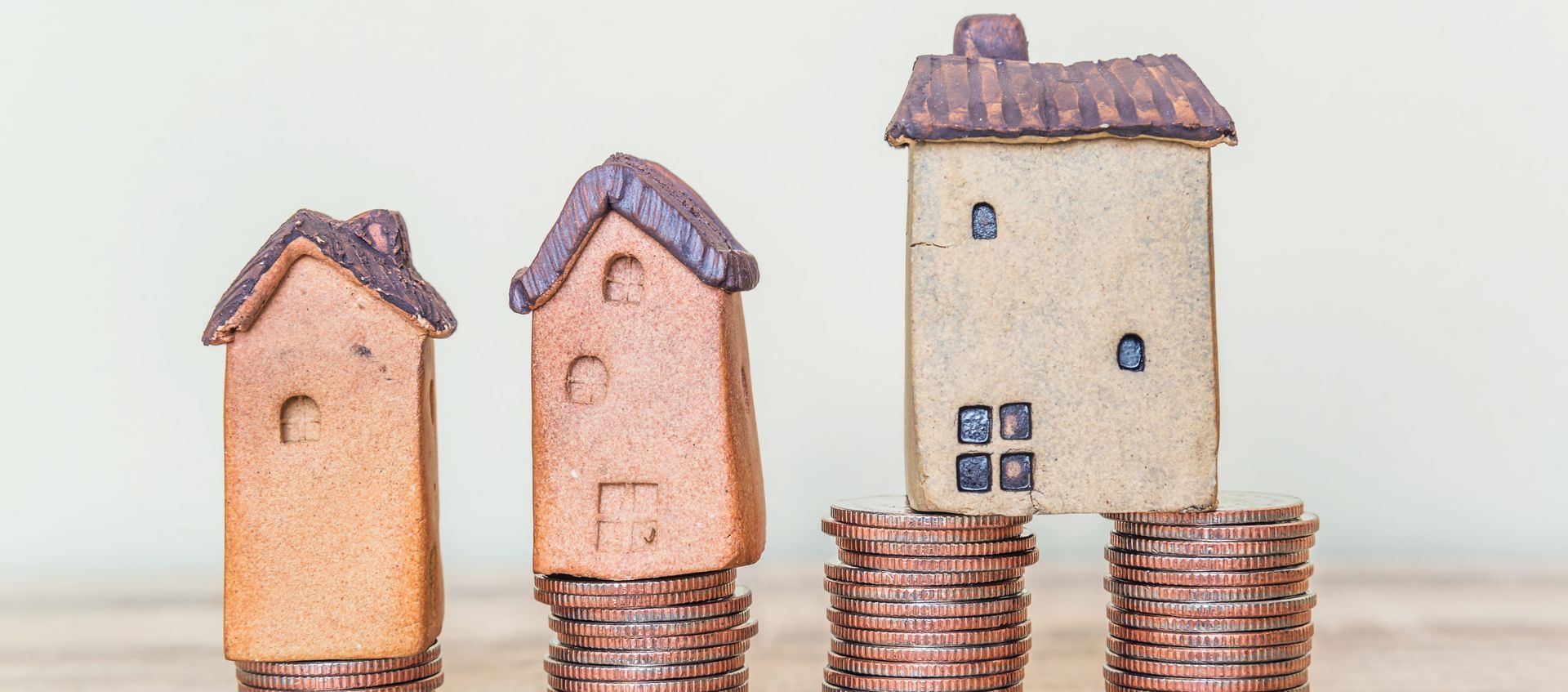 Three toy houses stacked on piles of coins; a concept of financial growth.