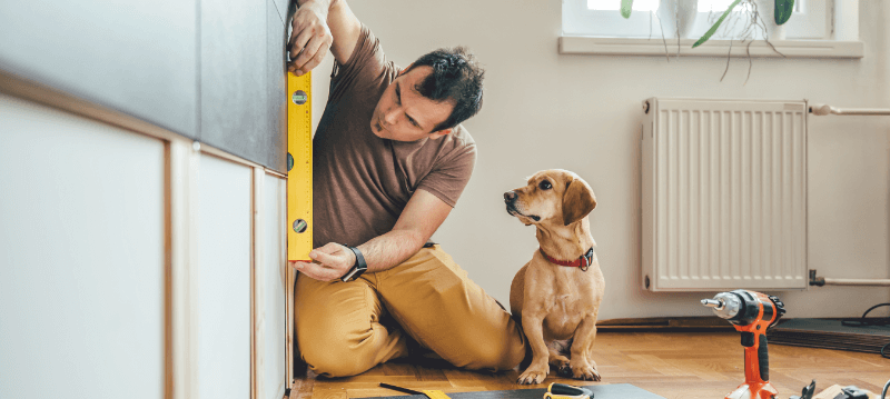Man using level while dog watches in a home setting.