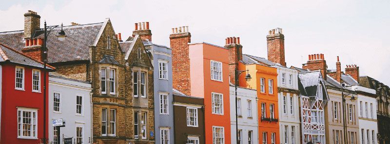 Row of colorful townhouses with chimneys against a pale sky.