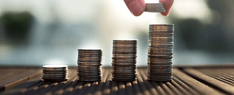Hand adding a coin to the top of a stack of coins, with three other shorter stacks.