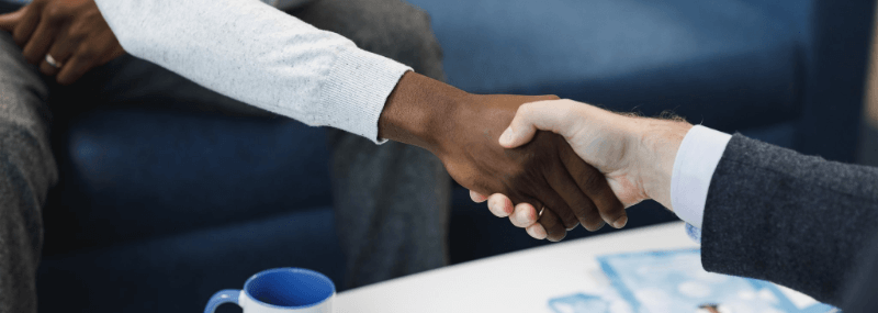Two people shaking hands in a business setting; one person is Black, the other is white.
