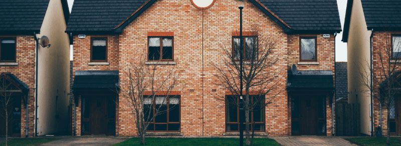 Row of brick townhouses with dark roofs and small trees in front.
