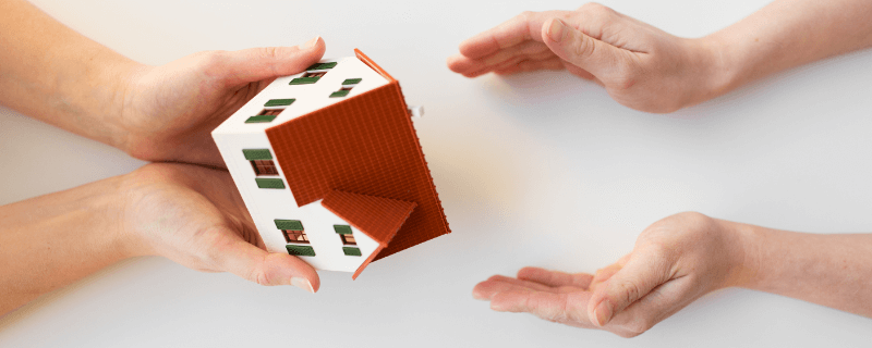 Hands passing a paper house, symbolizing property transfer or real estate.