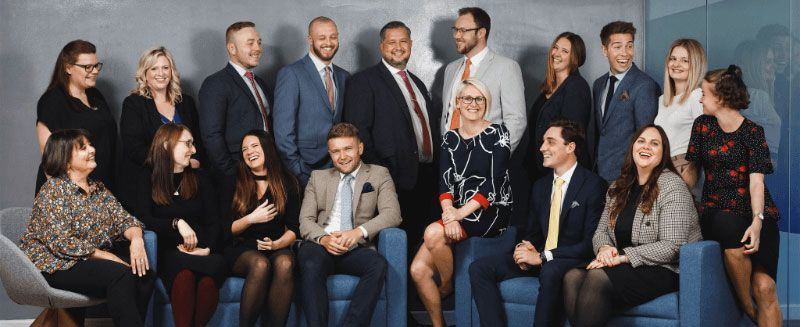 Group of smiling people posing for a professional photo, wearing suits and business attire.