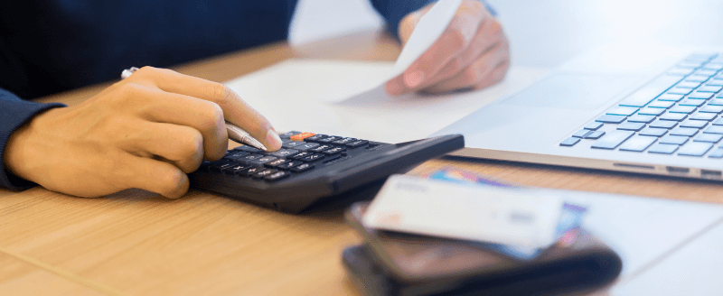 Person calculating expenses with a calculator, holding a bill, and with a laptop and credit card nearby.