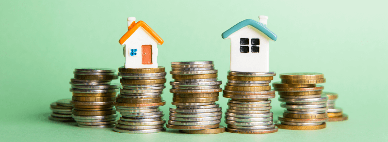 Two toy houses sit atop stacks of coins, symbolizing real estate investment.