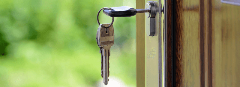 Keys in a lock on a wooden door, with a green, blurred background.
