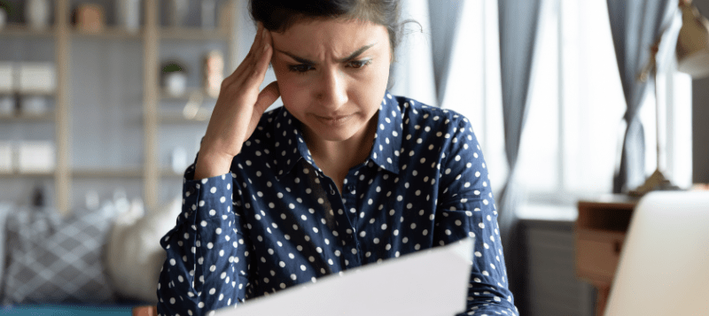 Woman with hand on head, looking stressed while reading a document.