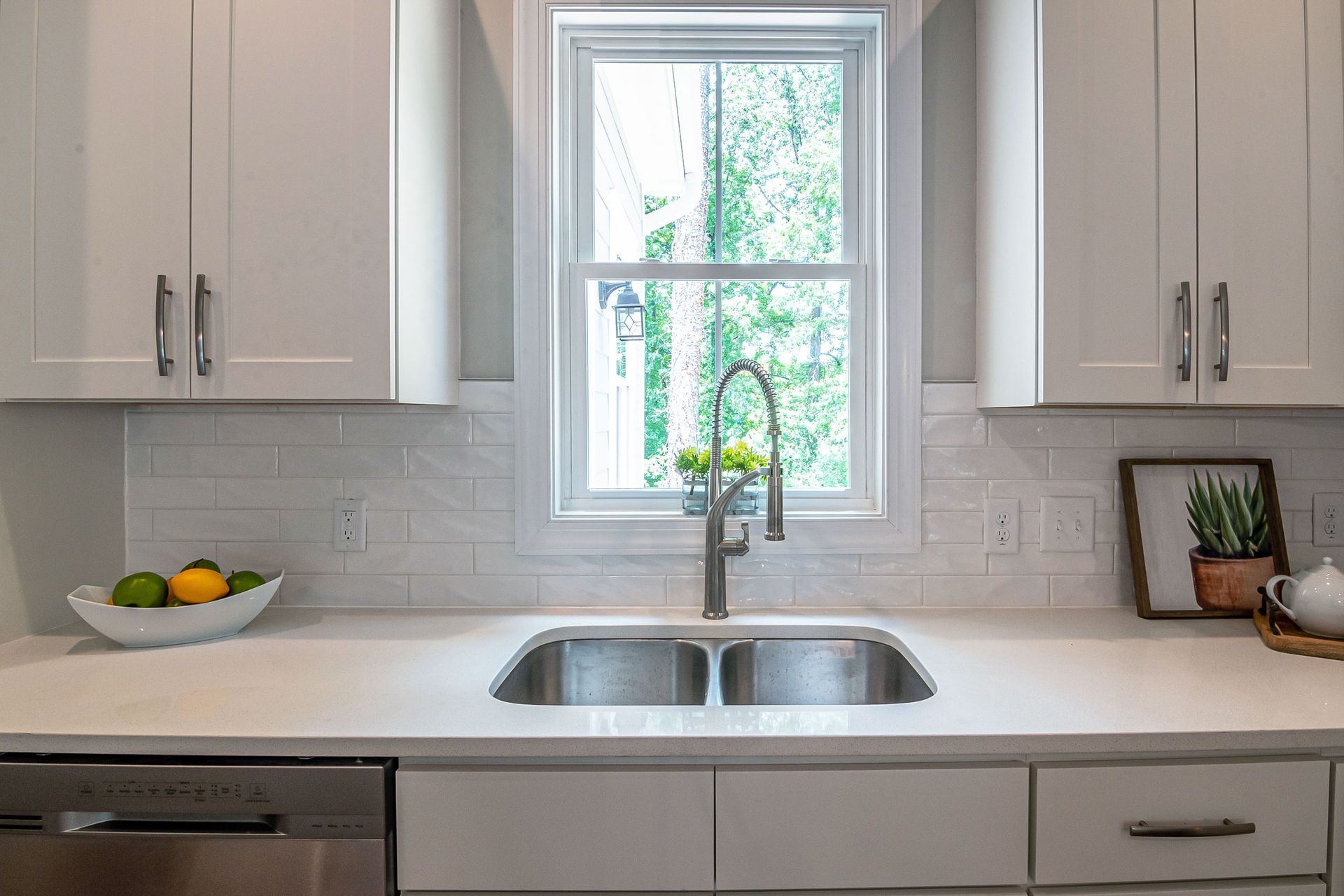 Bright kitchen with white cabinets, window above sink, and fruit bowl on the counter.