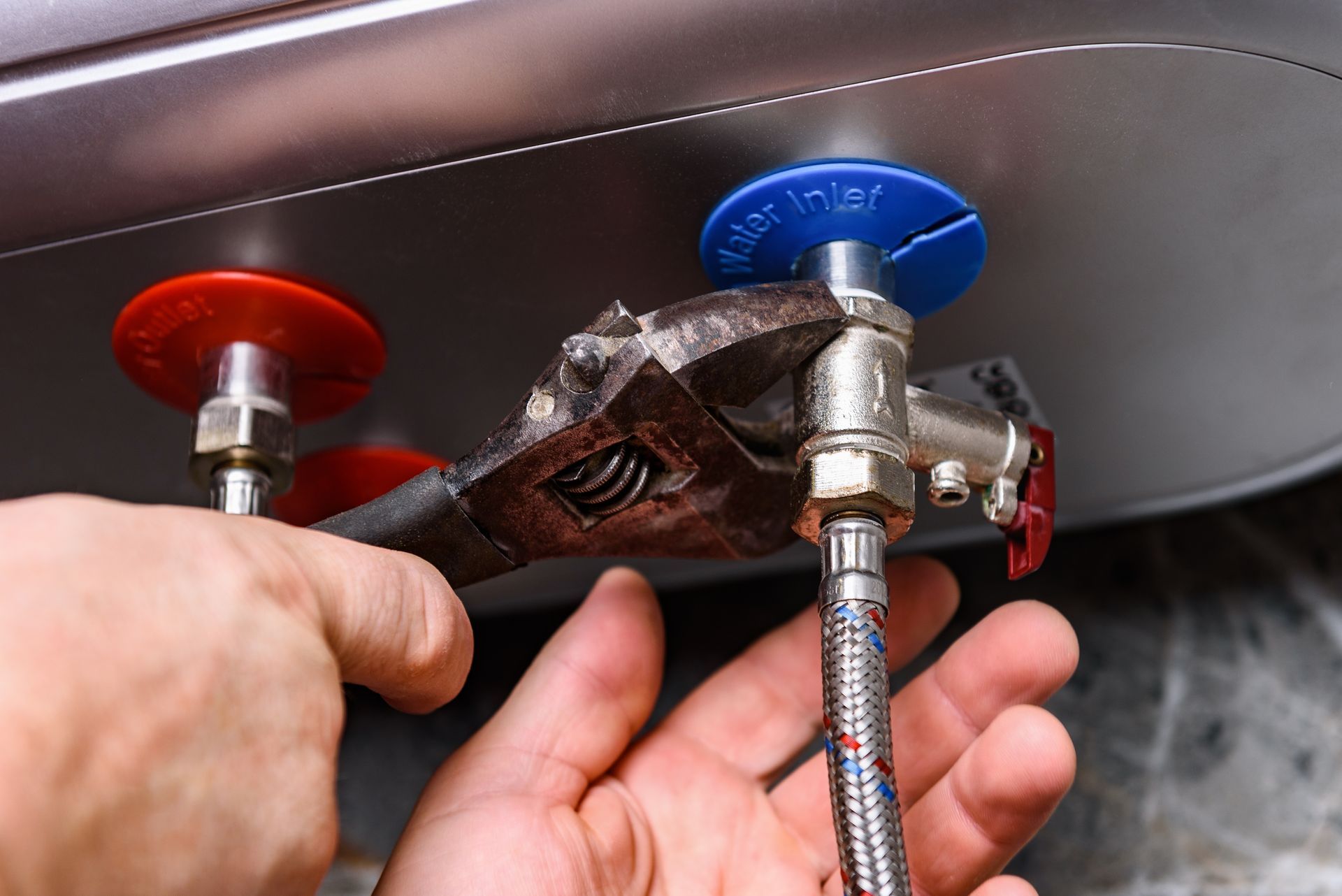 Hands tightening plumbing fittings under a sink with red and blue shutoff valves.