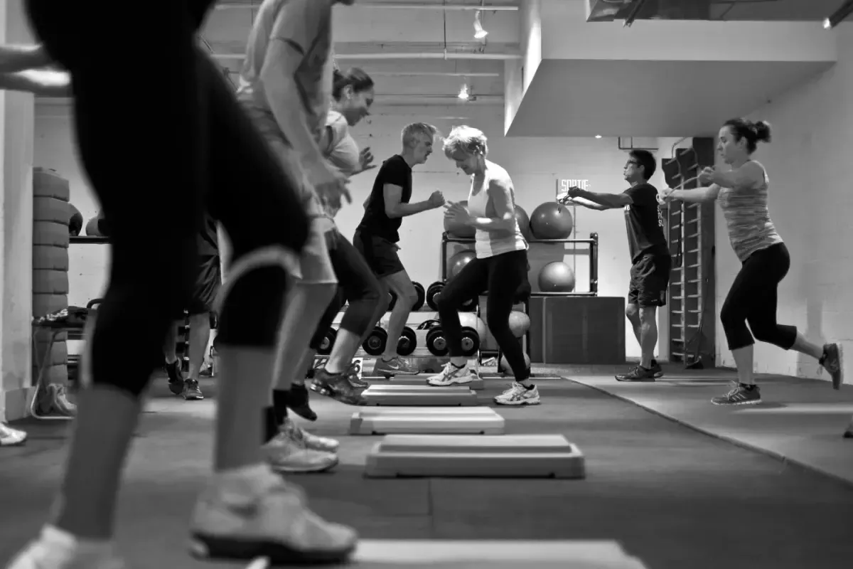 Cours collectif de fitness avec des participants qui pratiquent le step dans une salle de sport, autour de plateformes.