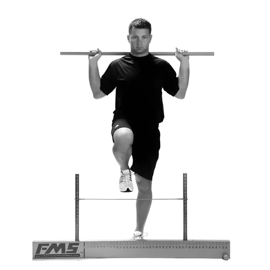 Homme en équilibre sur une jambe, une barre posée sur les épaules, sur une plateforme d’entraînement