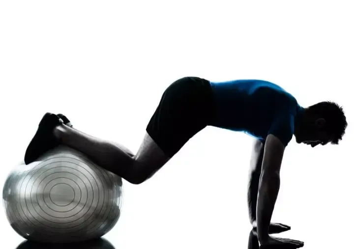Personne en position de planche, les pieds posés sur un ballon de gym, sur fond blanc