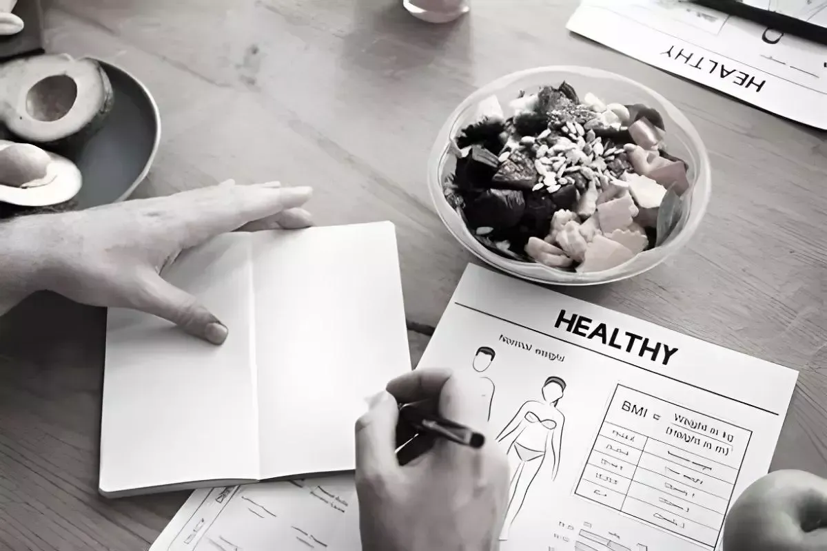 Personne écrivant sur une fiche « HEALTHY », à côté d’un bol de salade posé sur un bureau