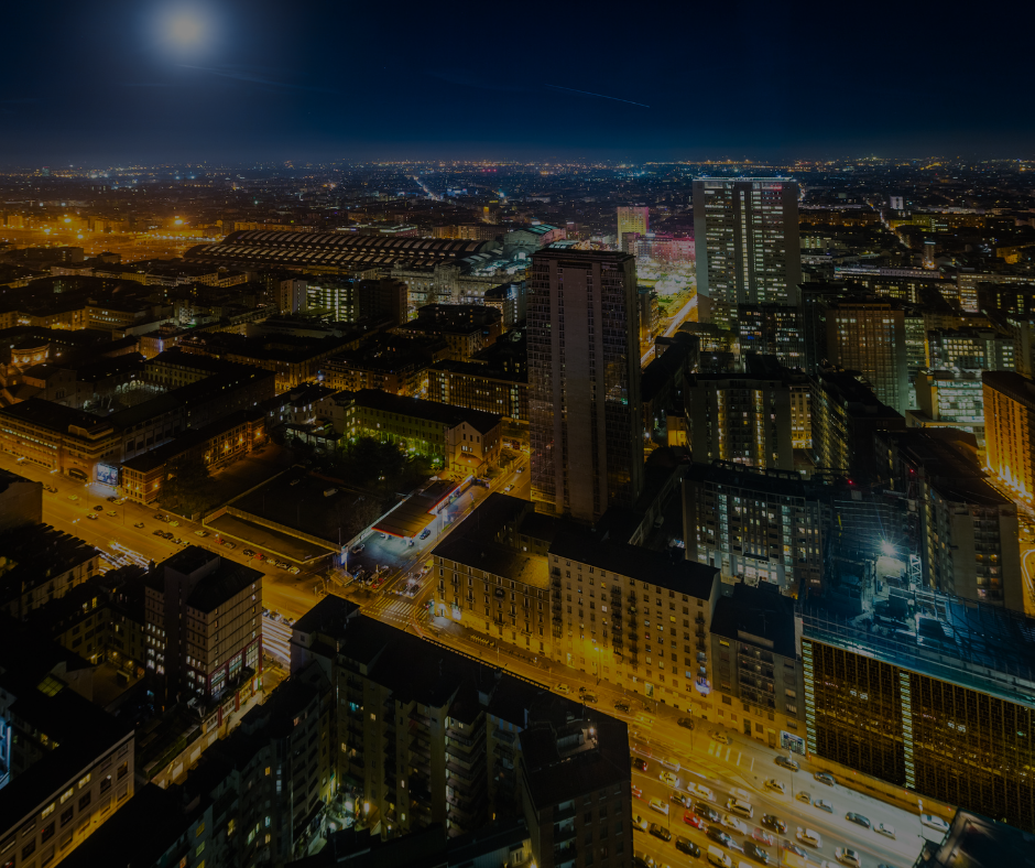 Una veduta notturna dall'alto di uno skyline cittadino densamente illuminato, caratterizzato da alti edifici e lampioni scintillanti.