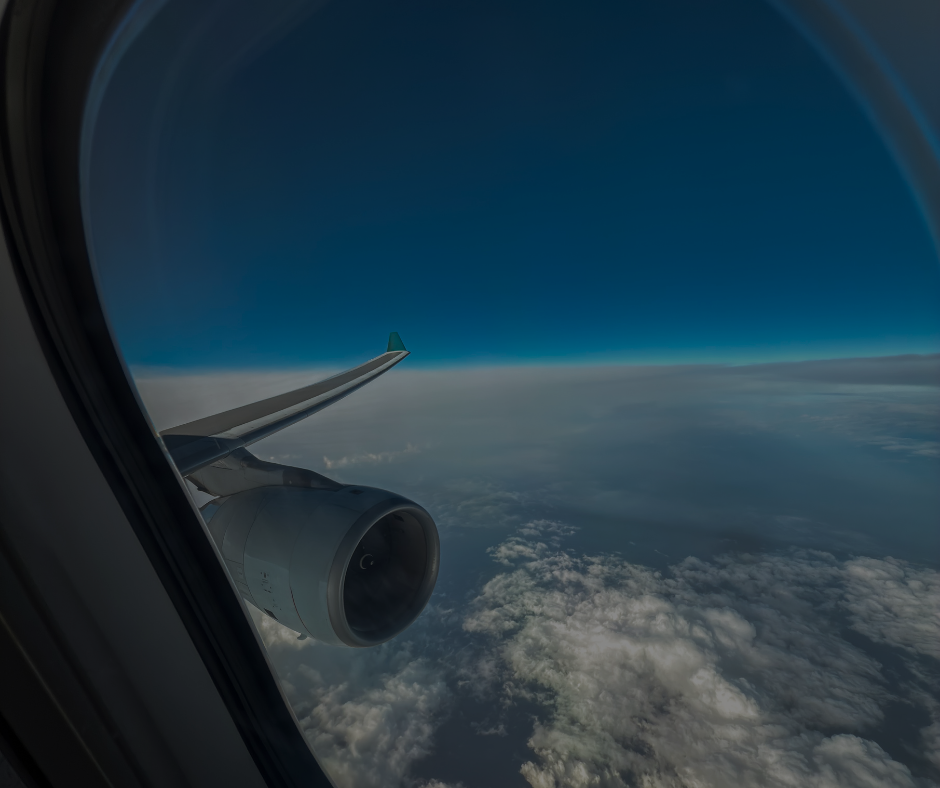 Vista dal finestrino di un aereo che mostra l'ala e il motore stagliarsi contro un cielo azzurro brillante e uno strato di nuvole sottostante.