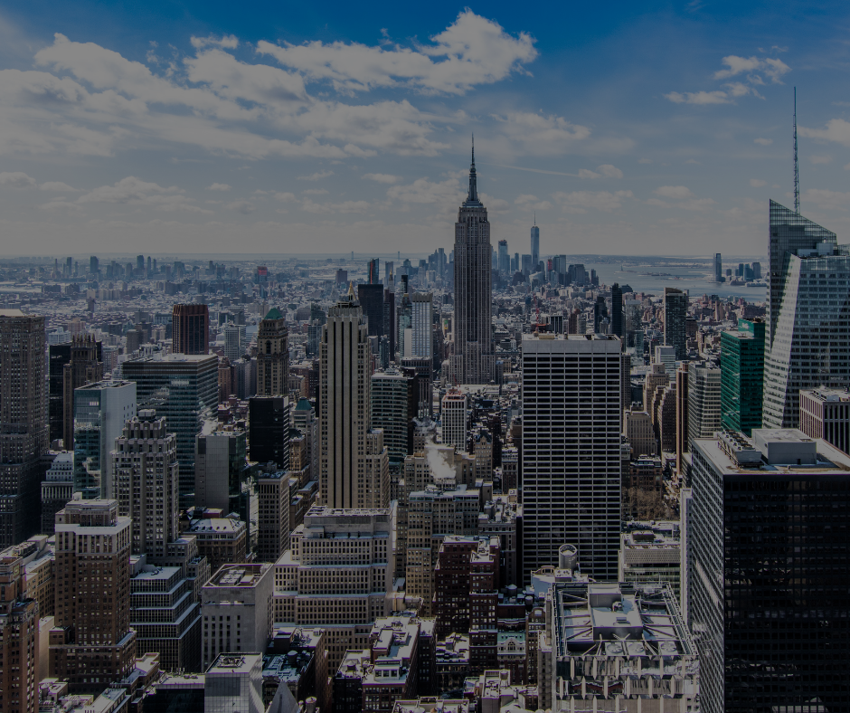 Una veduta dall'alto dello skyline di New York, con l'Empire State Building ben visibile sotto un cielo nuvoloso e luminoso.