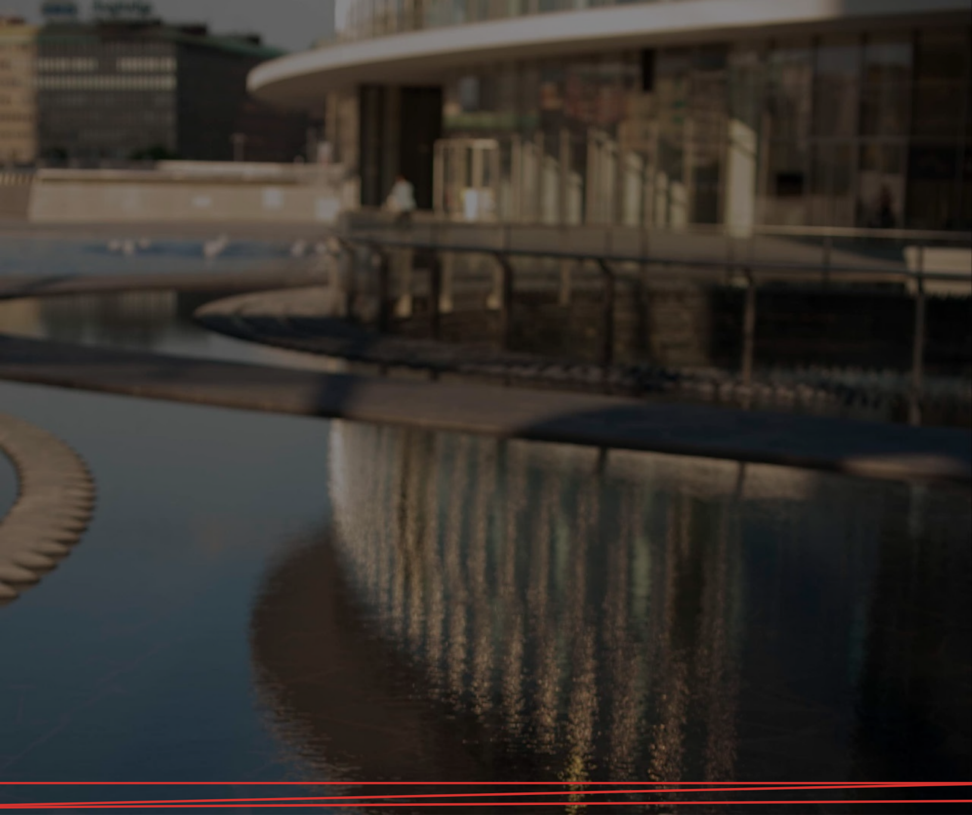 Un moderno edificio dalle linee curve si riflette in una calma e scura pozza d'acqua al crepuscolo.