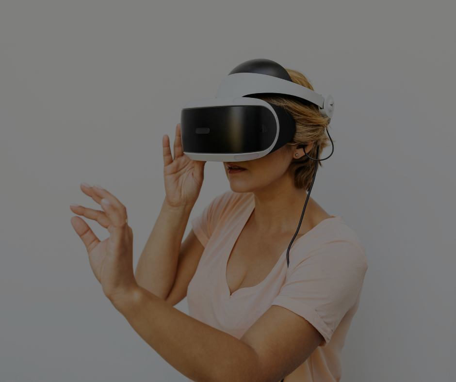Una persona indossa un visore VR bianco e nero e allunga la mano come se stesse interagendo con un ambiente virtuale sullo sfondo di una parete grigia.