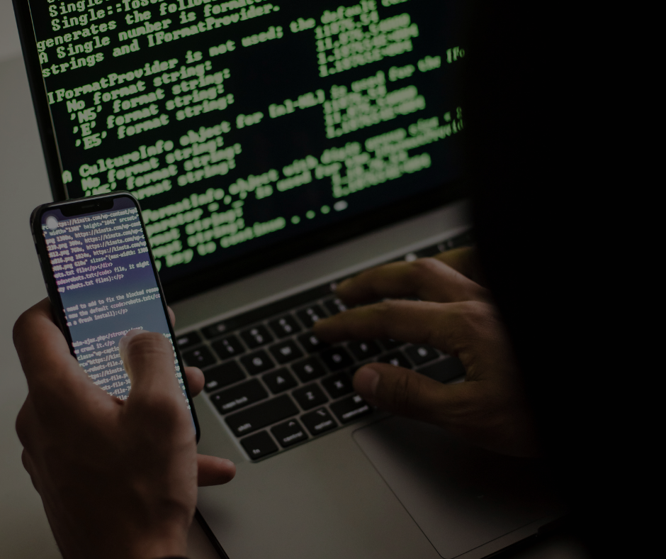 Una persona utilizza uno smartphone e un laptop che visualizzano righe di codice verde su uno sfondo scuro.