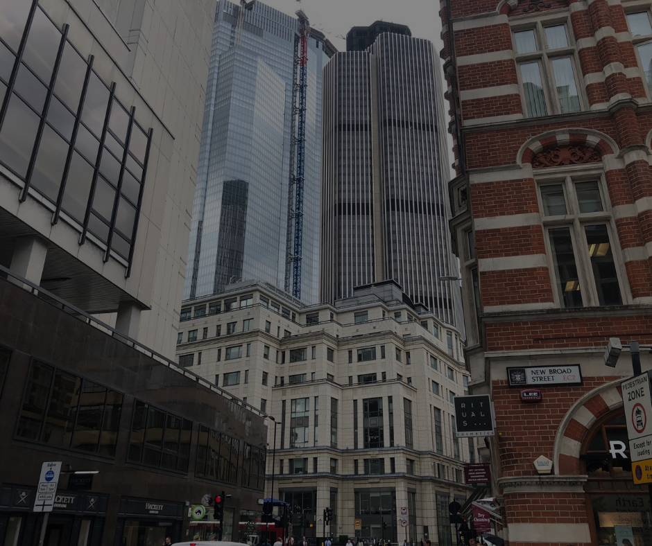 In una via di Londra, moderni grattacieli di vetro svettano alle spalle di edifici più antichi in pietra e mattoni rossi.