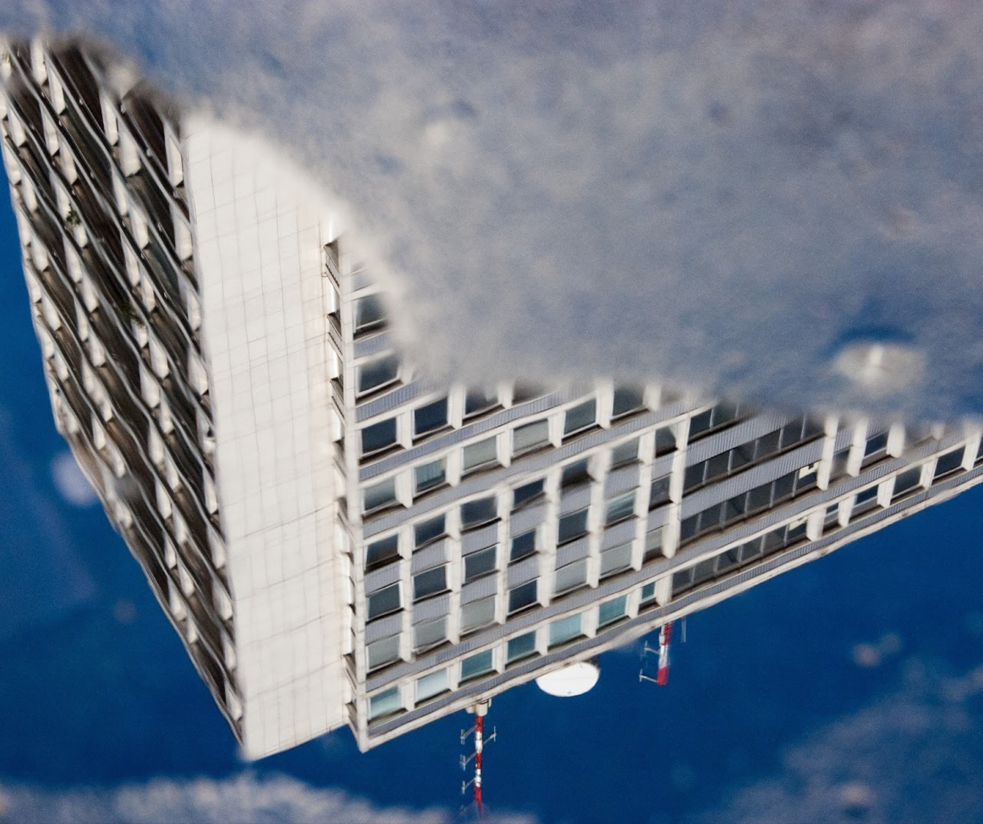 Il riflesso capovolto di un alto edificio bianco con molte finestre in una pozza d'acqua sotto un cielo azzurro e limpido.