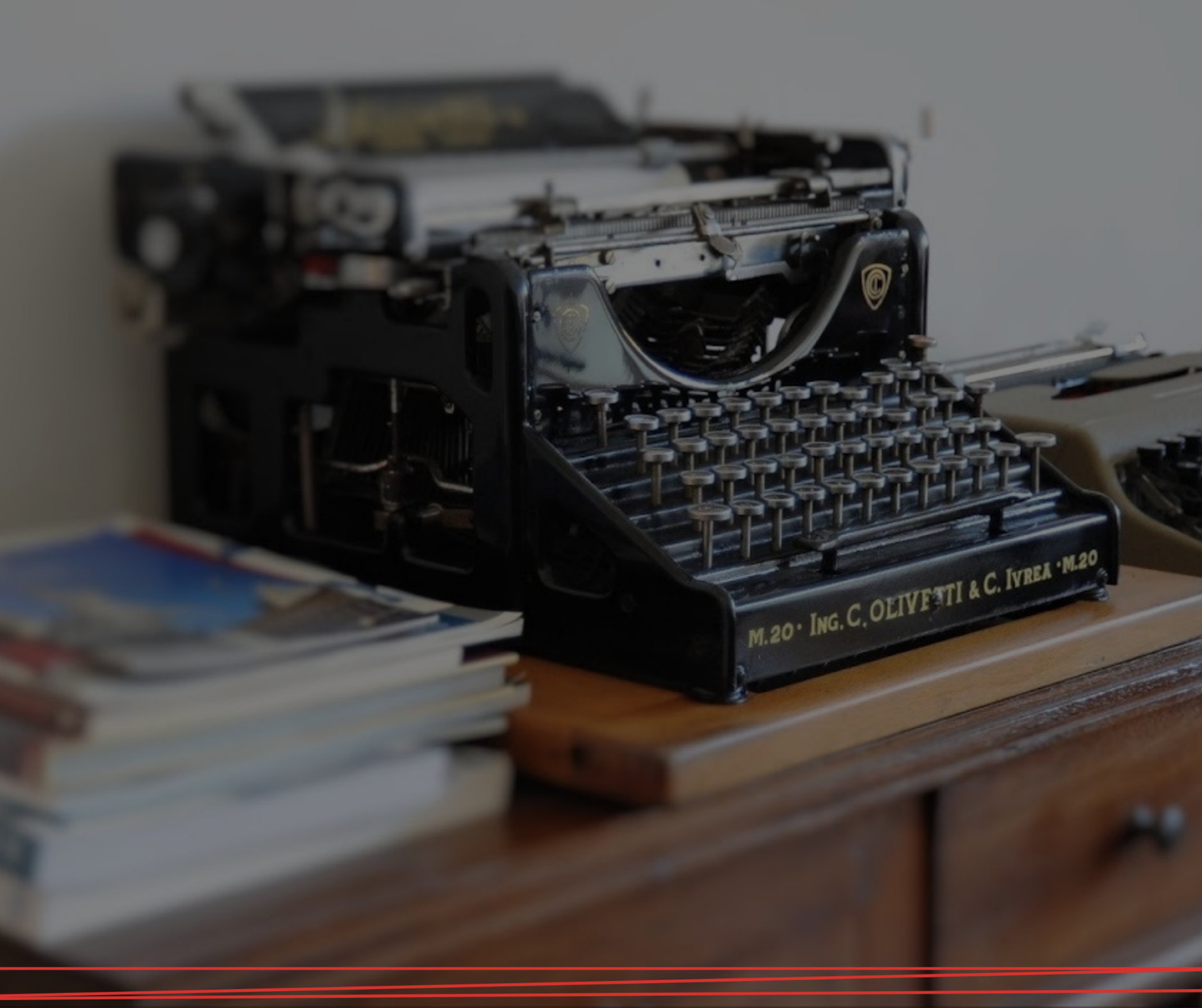 Una macchina da scrivere nera d'epoca è appoggiata su una scrivania di legno accanto a una pila di libri.