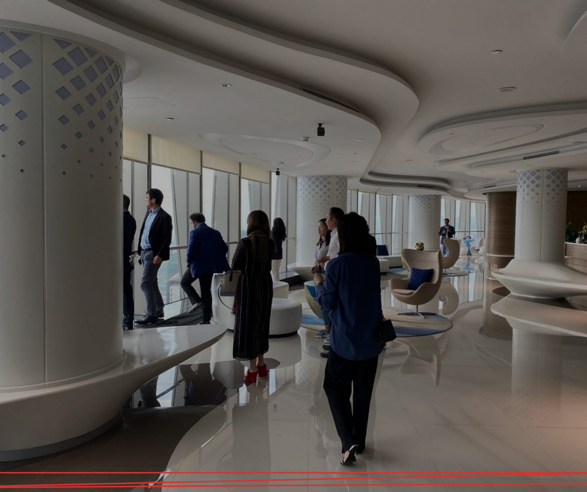 Le persone si fermano e camminano in una moderna lounge in un grattacielo, caratterizzata da un'architettura curvilinea, pilastri bianchi e ampie vetrate.