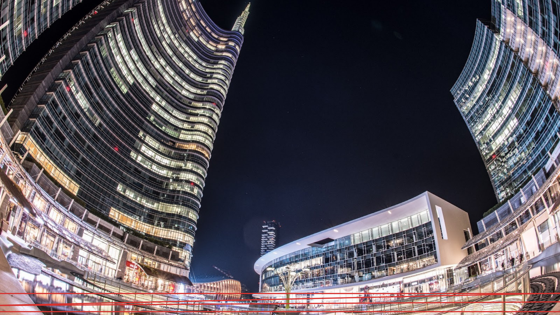 Vista notturna, dal basso e grandangolare, dei moderni grattacieli illuminati di Piazza Gae Aulenti a Milano.